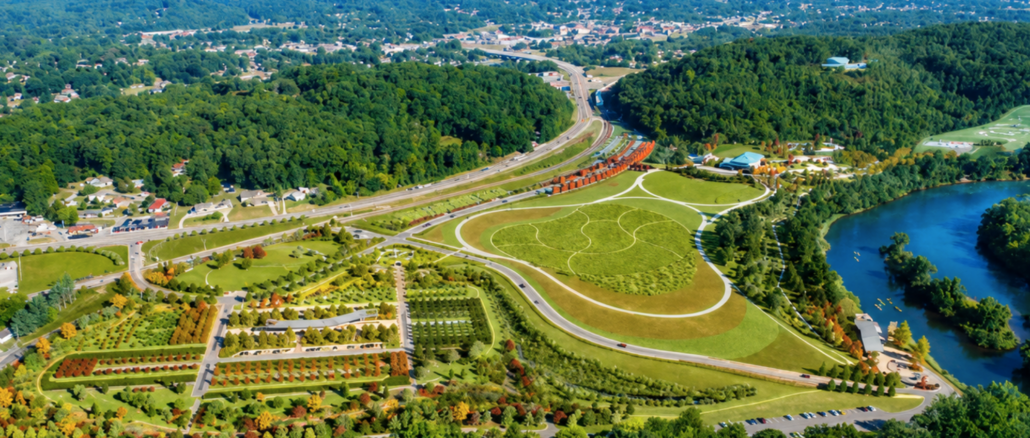 Aerial view of a large park with winding paths, roads, and a surrounding forest near a river edge.