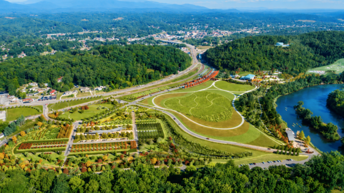 Aerial view of a large park with winding paths, roads, and a surrounding forest near a river edge.